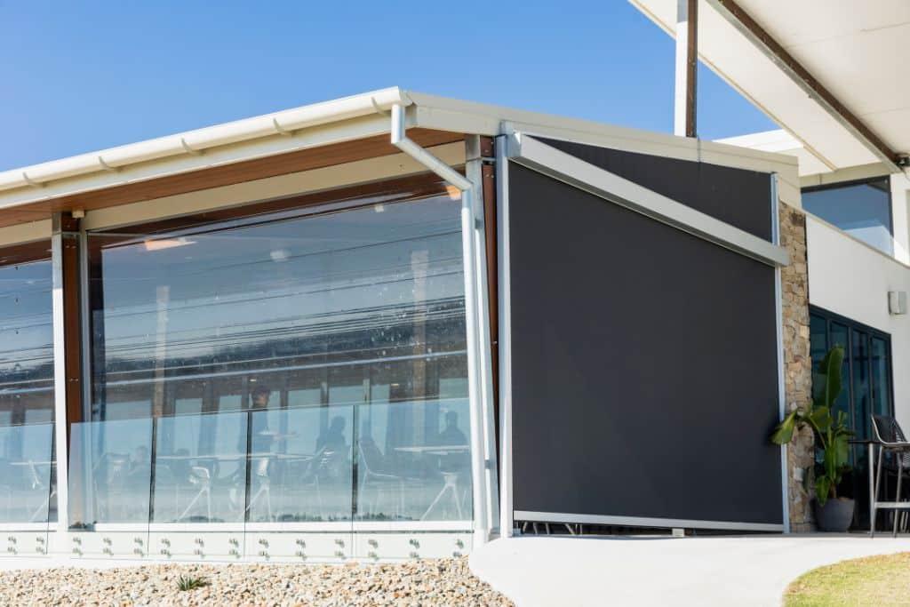 Modern café with glass walls and a large black outdoor retractable blind, providing sun protection and wind resistance.